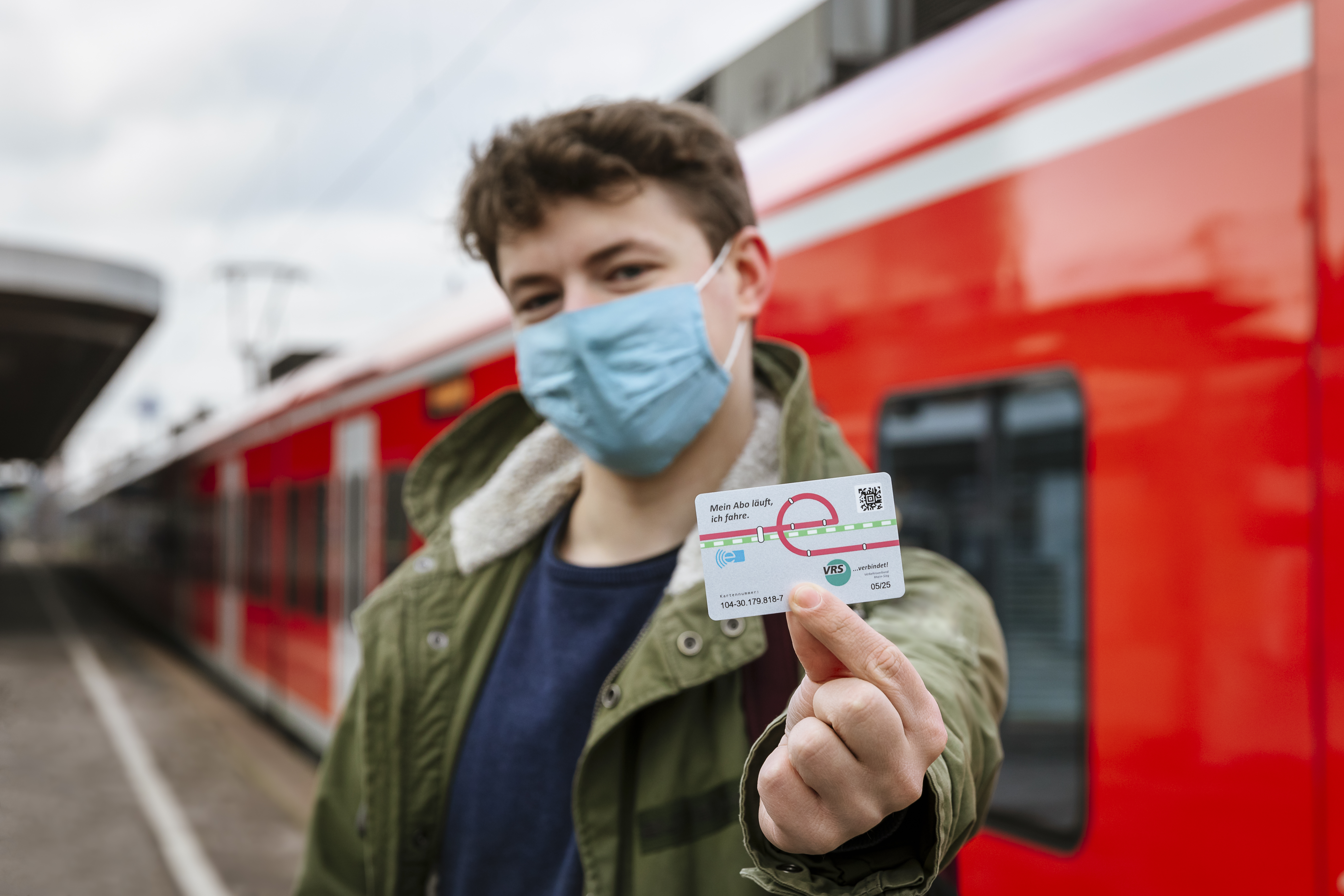 Ein Bild zeigt einen jungen männlichen Fahrgast, der das Jobticket light in die Kamera hält. Unter seiner Maske scheint er zu lächeln.